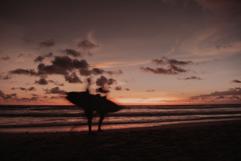 Surfers carrying boards along Santa Teresa beach at sunset