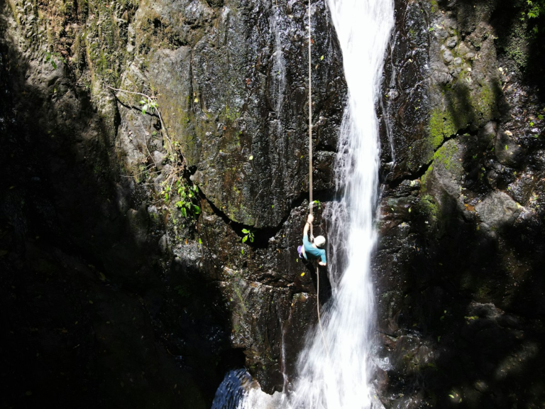 Person rappelling beside a waterfall; activity illustration