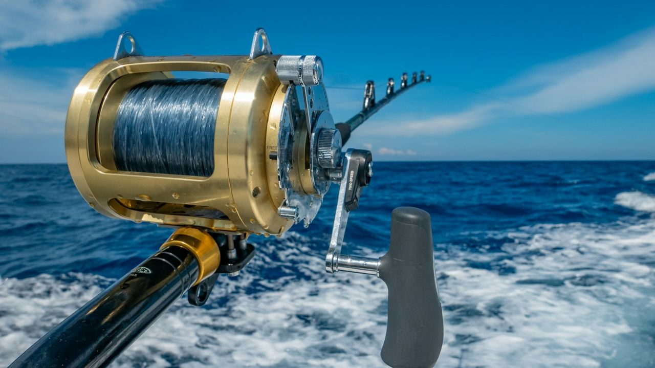 Gold fishing reel and rod above deep blue water
