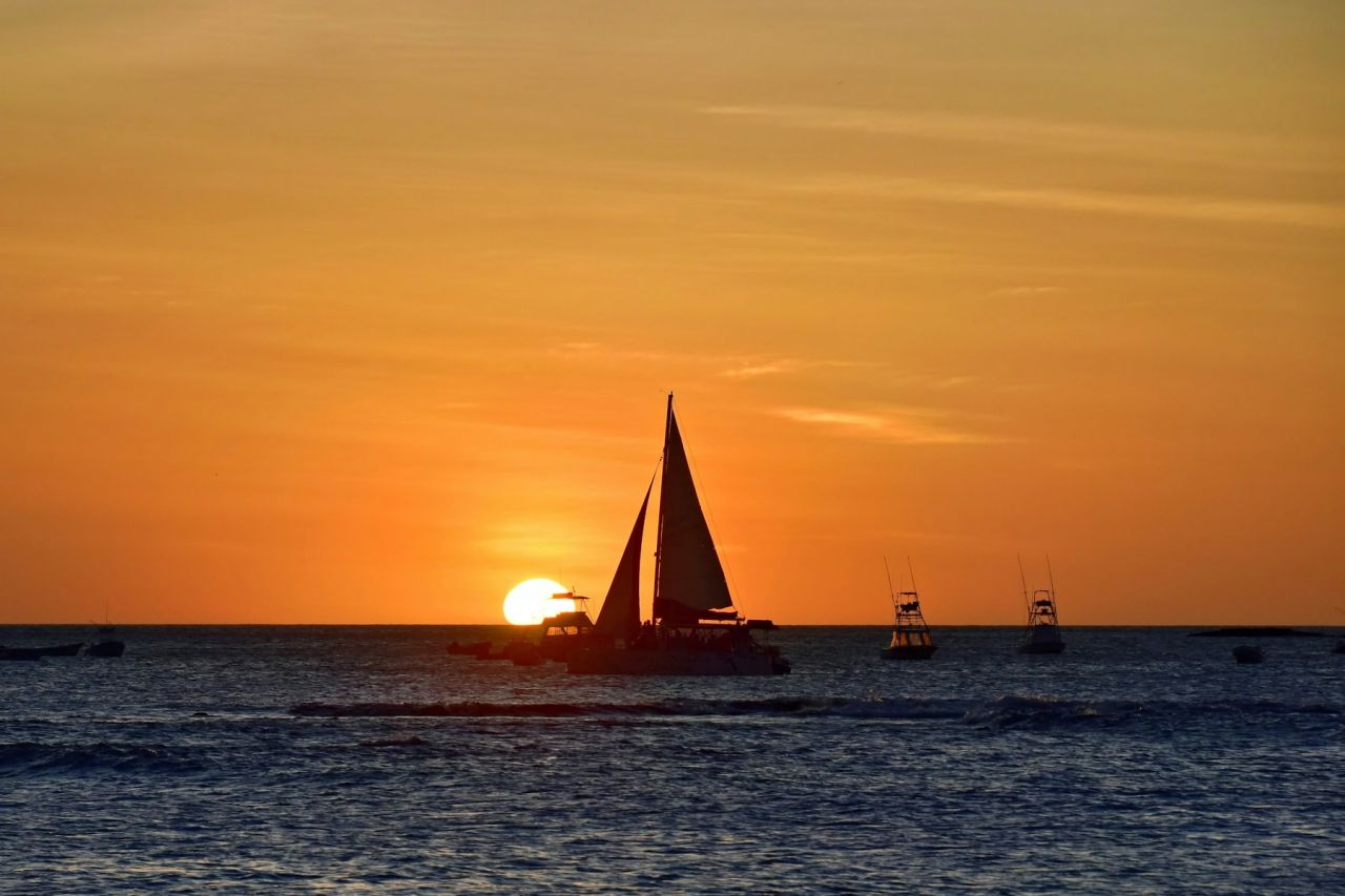 A sailing vessel silhouetted against an orange sunset; sailing experience illustration